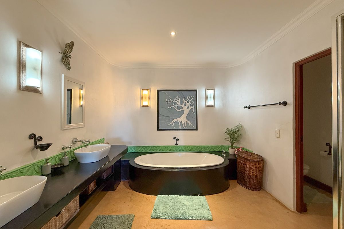Spacious bathroom featuring a built-in oval soaking tub, dual vessel sinks on a dark vanity, and decorative wall sconces.