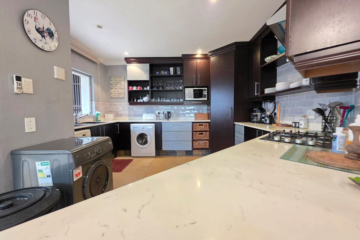 A functional kitchen featuring dark cabinetry, stone-look countertops, a subway tile backsplash, and integrated laundry appliances.
