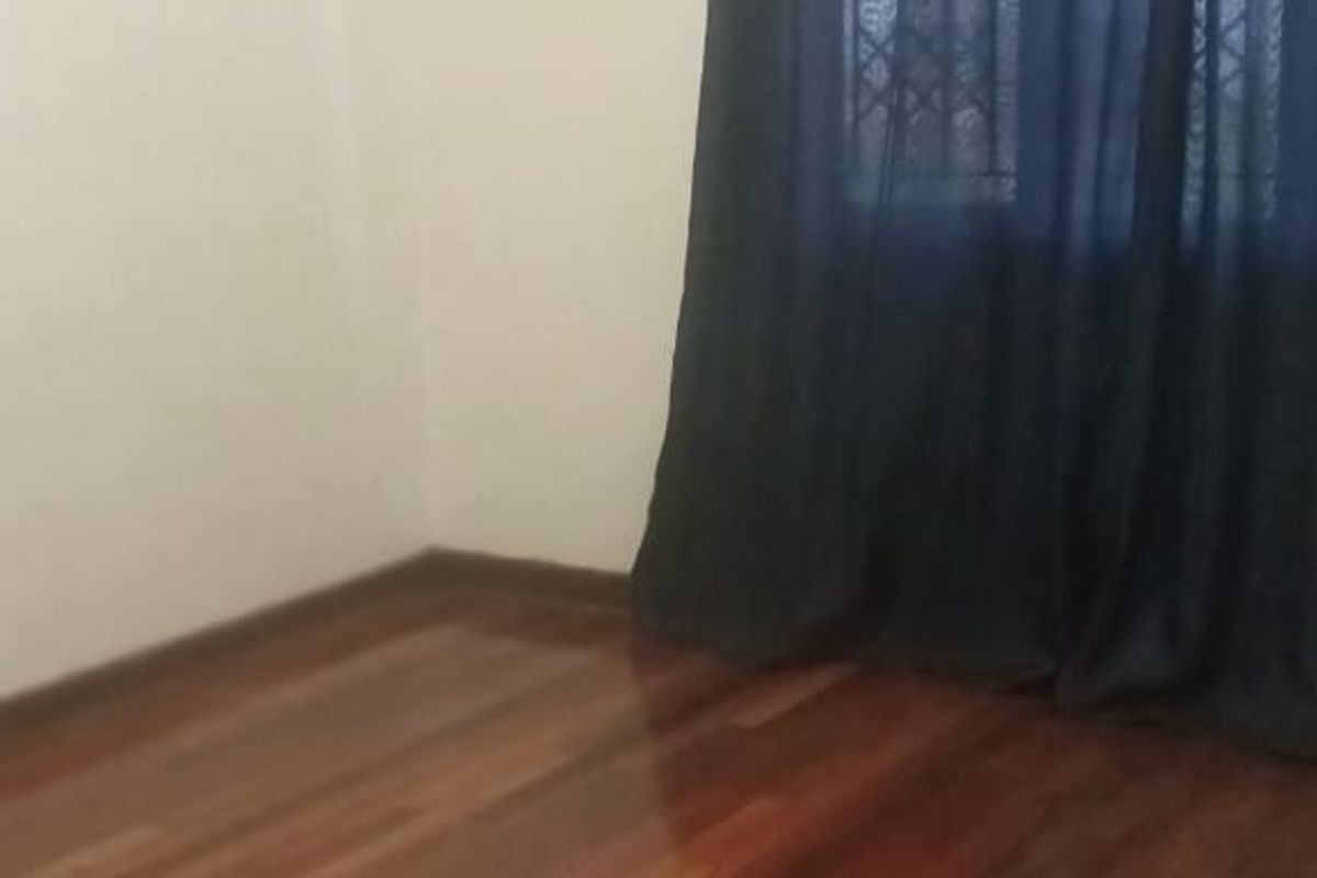 A bright, empty bedroom featuring polished hardwood timber flooring, high ceilings with decorative cornicing, and a window fitted with security bars.