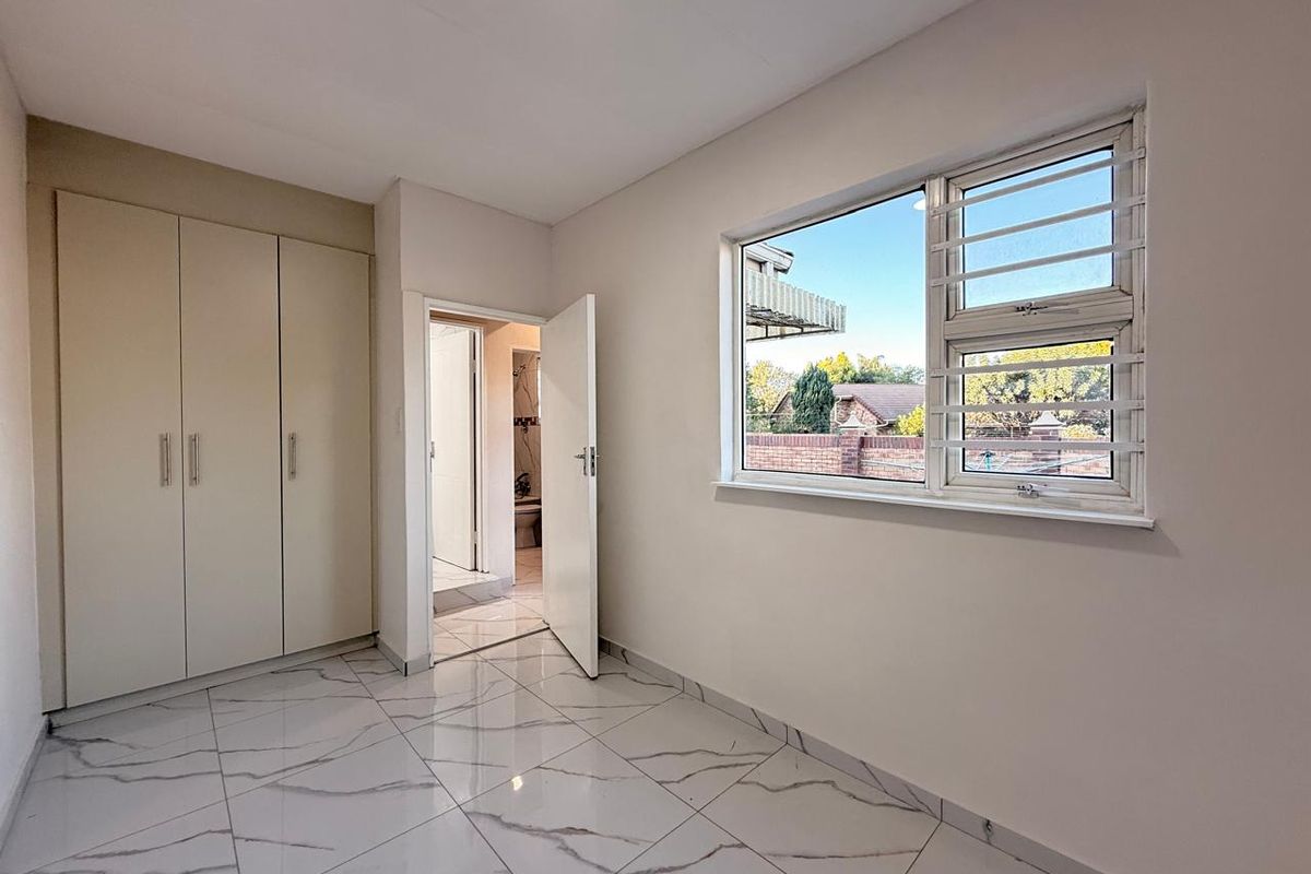 A bright, empty bedroom featuring modern marble-look floor tiles, built-in cupboards, and an adjoining en-suite bathroom.