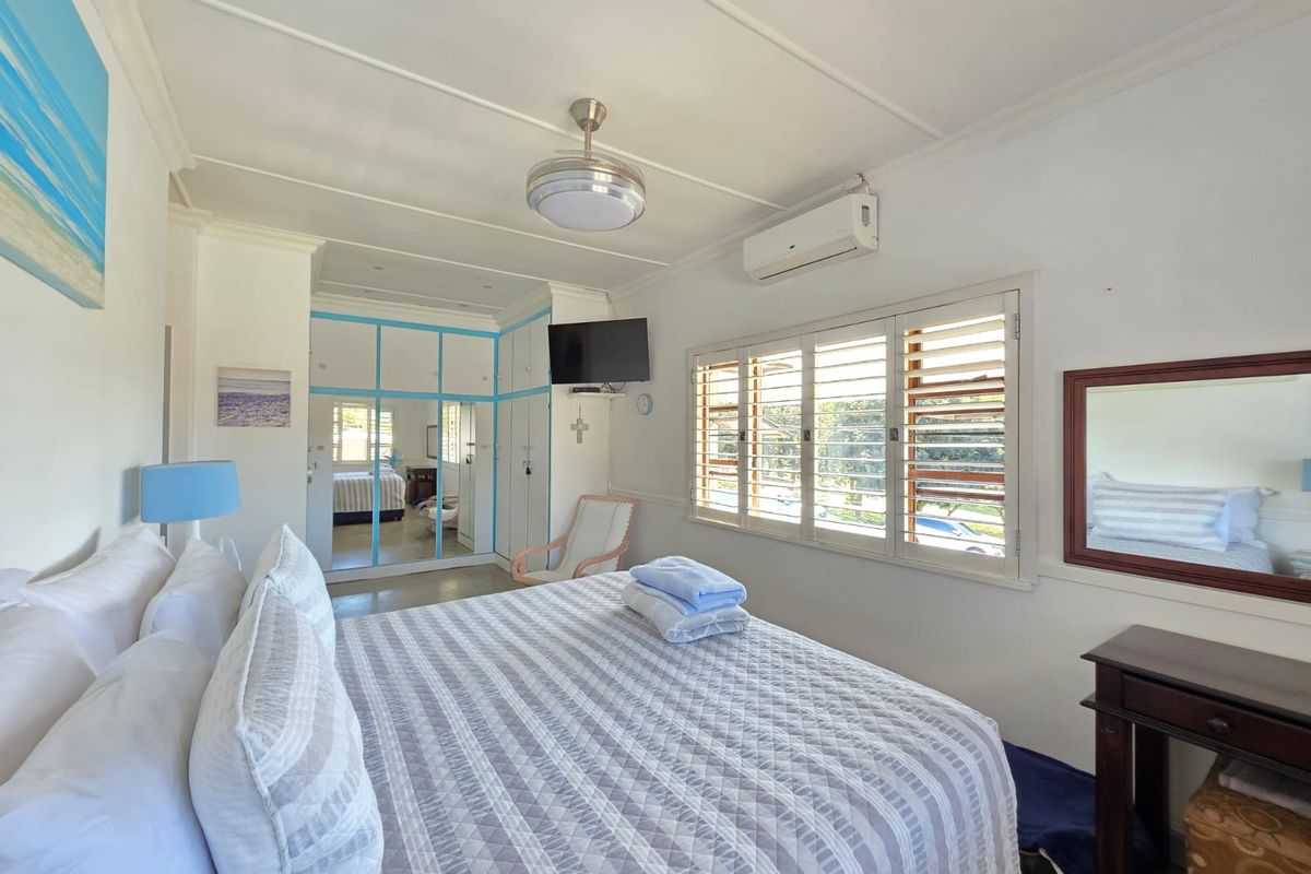 A bedroom featuring built-in mirrored wardrobes with blue trim, plantation-style window shutters, and a wall-mounted air conditioning unit.