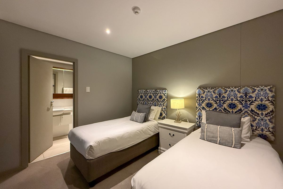 A well-maintained bedroom featuring neutral wall tones, plush carpeting, and an adjoining en-suite bathroom with modern vanity fixtures.