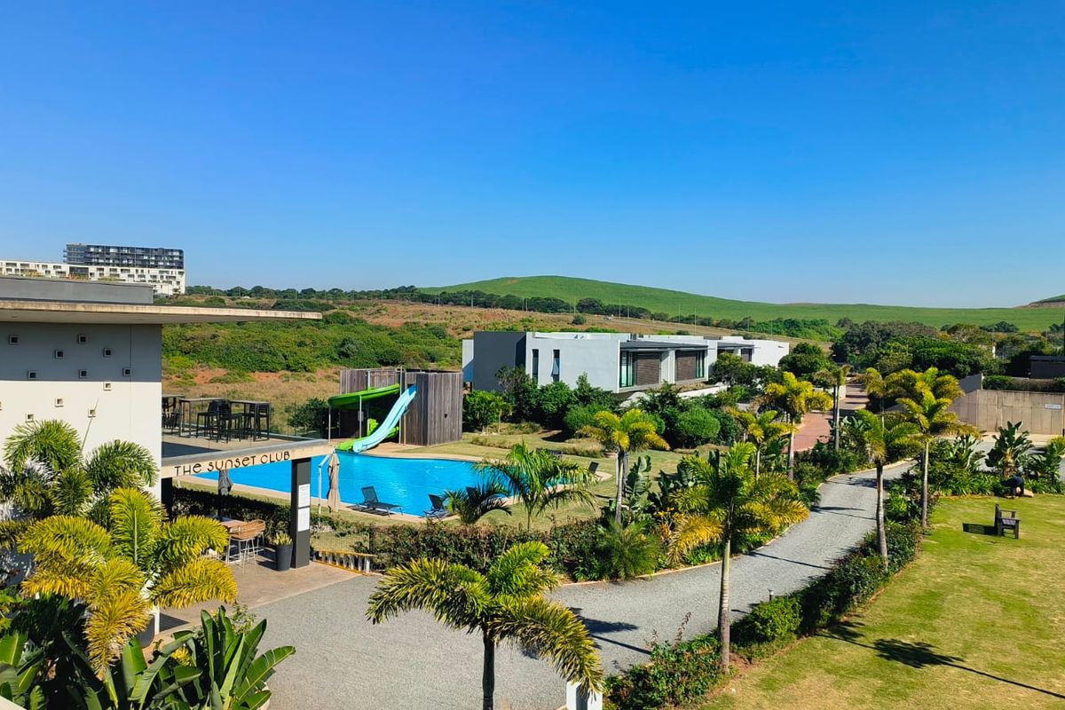 An elevated view of a residential estate featuring a swimming pool, landscaped gardens, and modern architectural buildings under a clear blue sky.