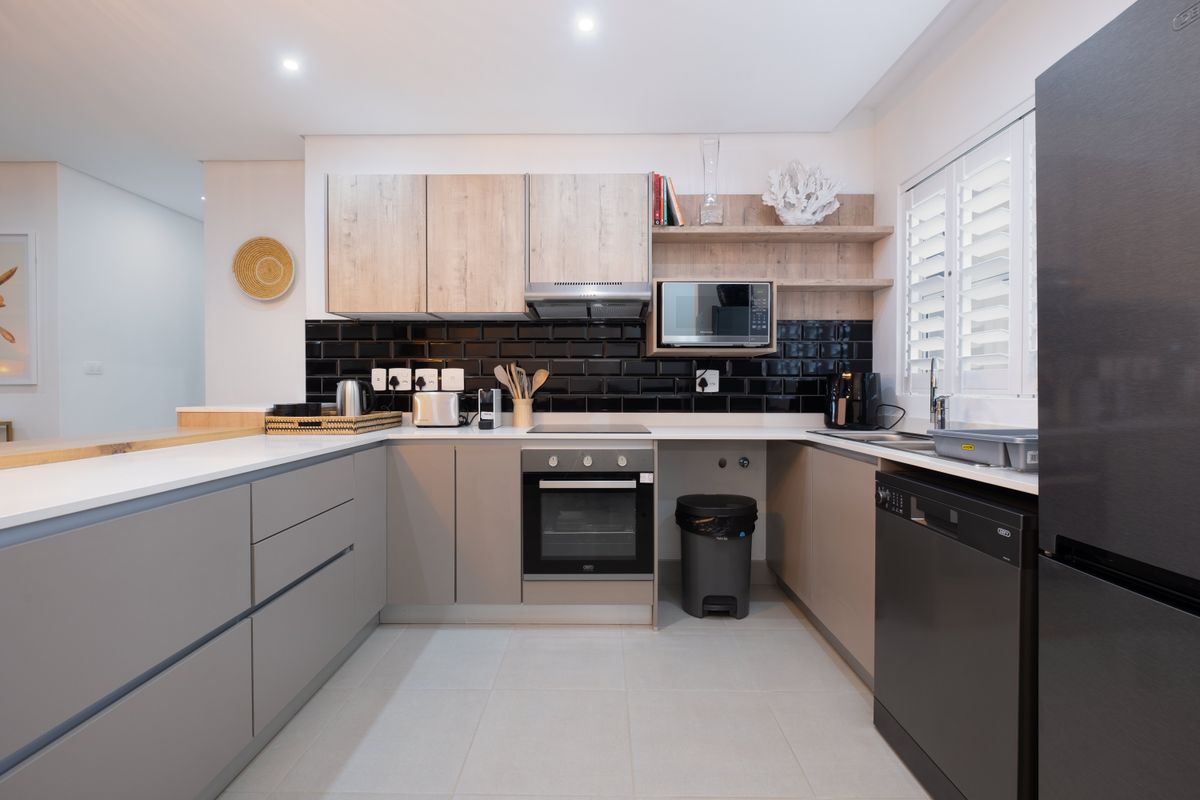 Modern kitchen featuring sleek grey cabinetry, black subway tile backsplash, stone countertops, integrated appliances, and high-quality finishes throughout.