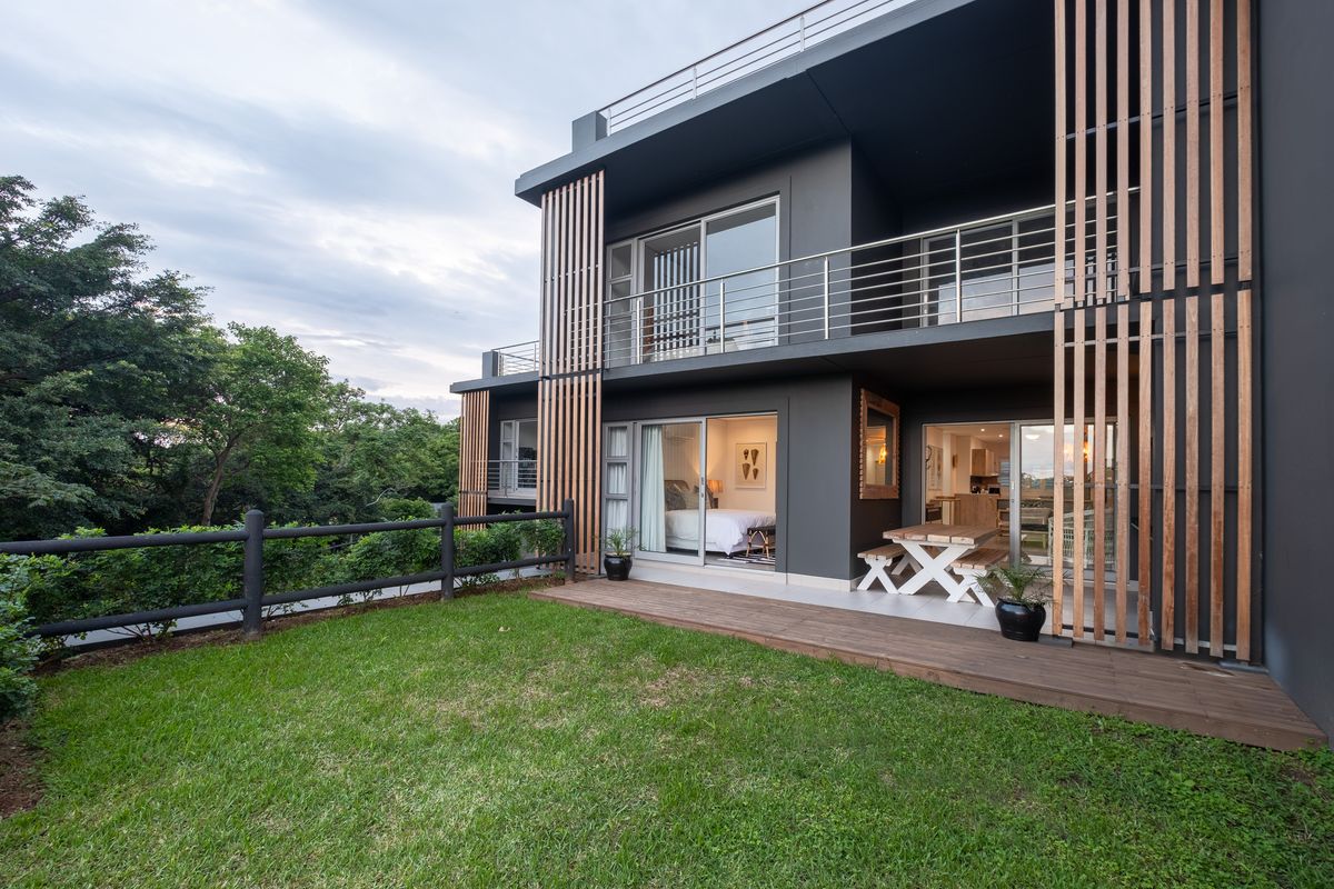 Modern apartment rear exterior featuring a timber deck, landscaped garden, and vertical timber privacy screens with access to ground floor living areas.