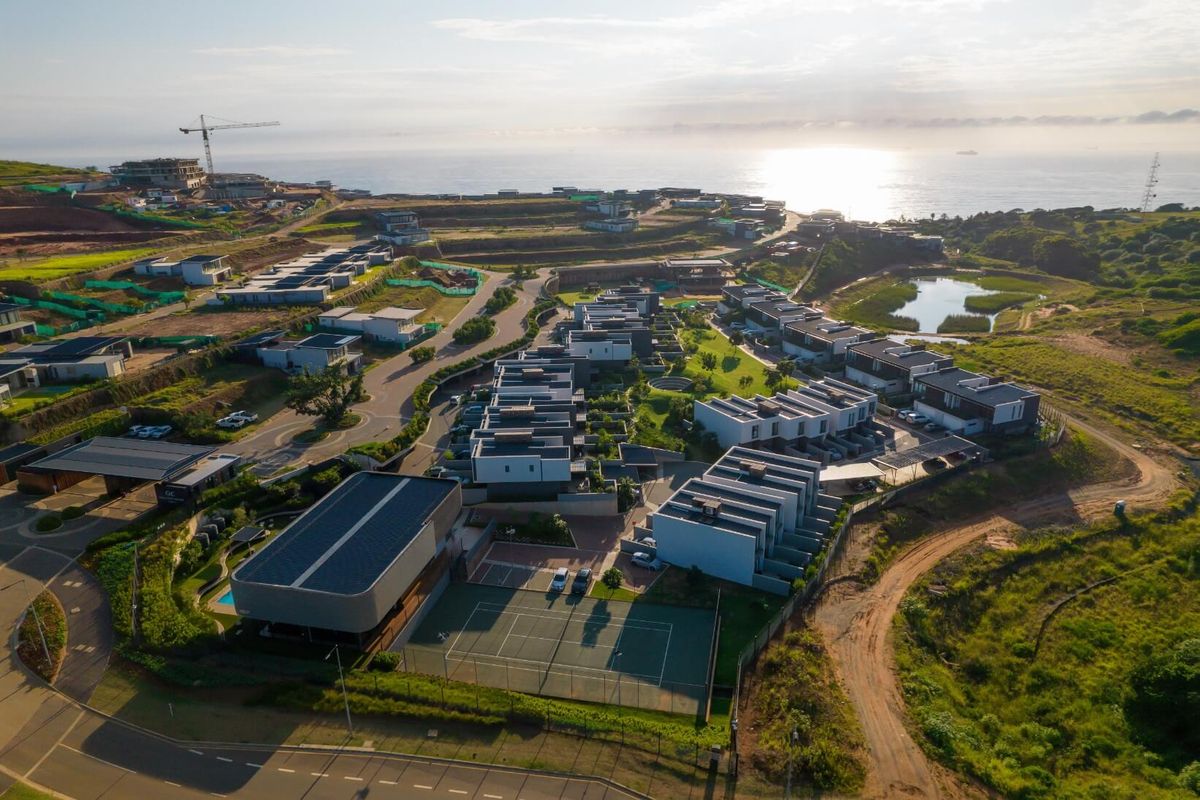 Aerial view of a modern residential estate featuring contemporary townhouses, a tennis court, and landscaped grounds overlooking the coastline.