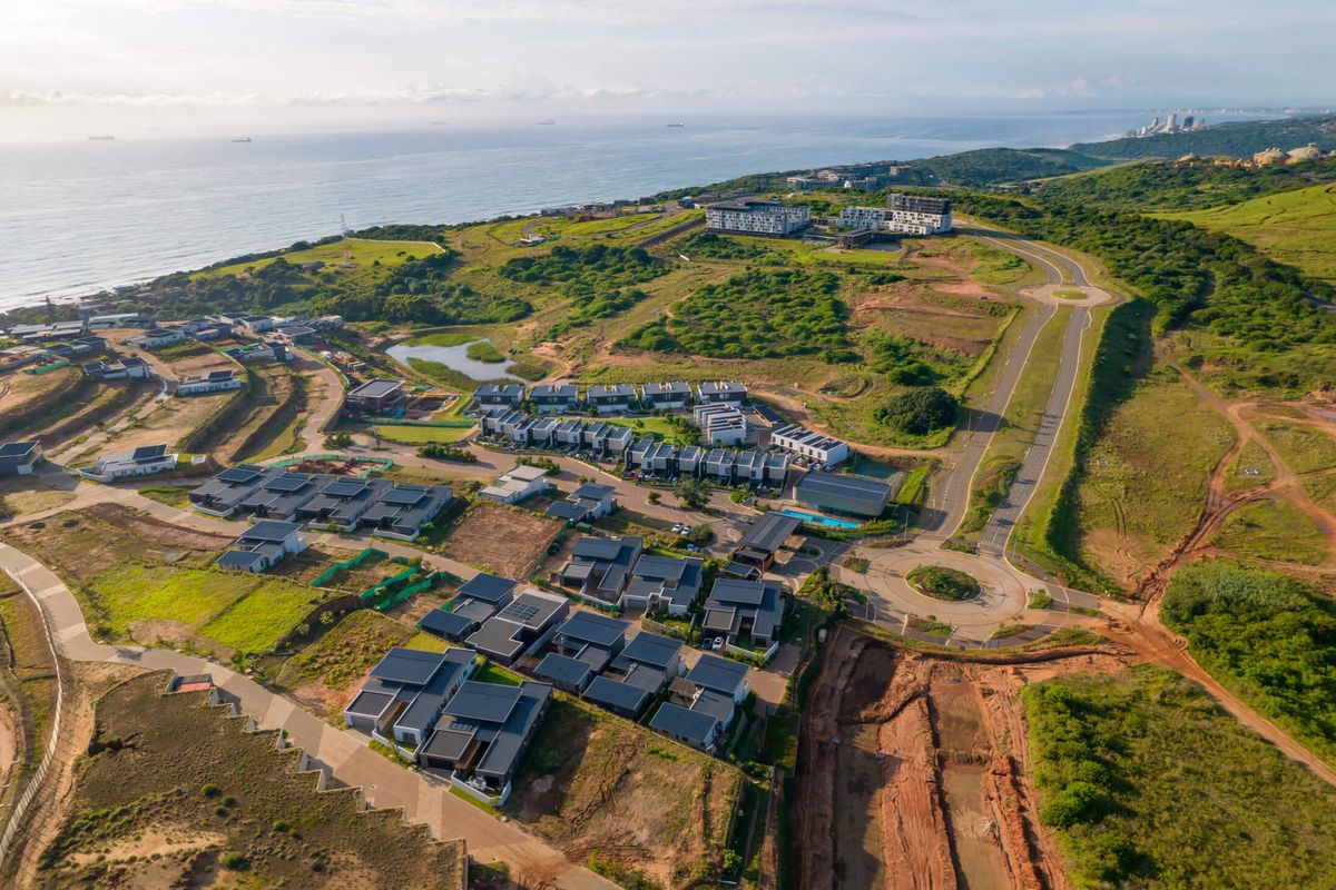 Aerial view of a coastal residential estate development featuring modern housing clusters, paved road infrastructure, and surrounding natural landscape.