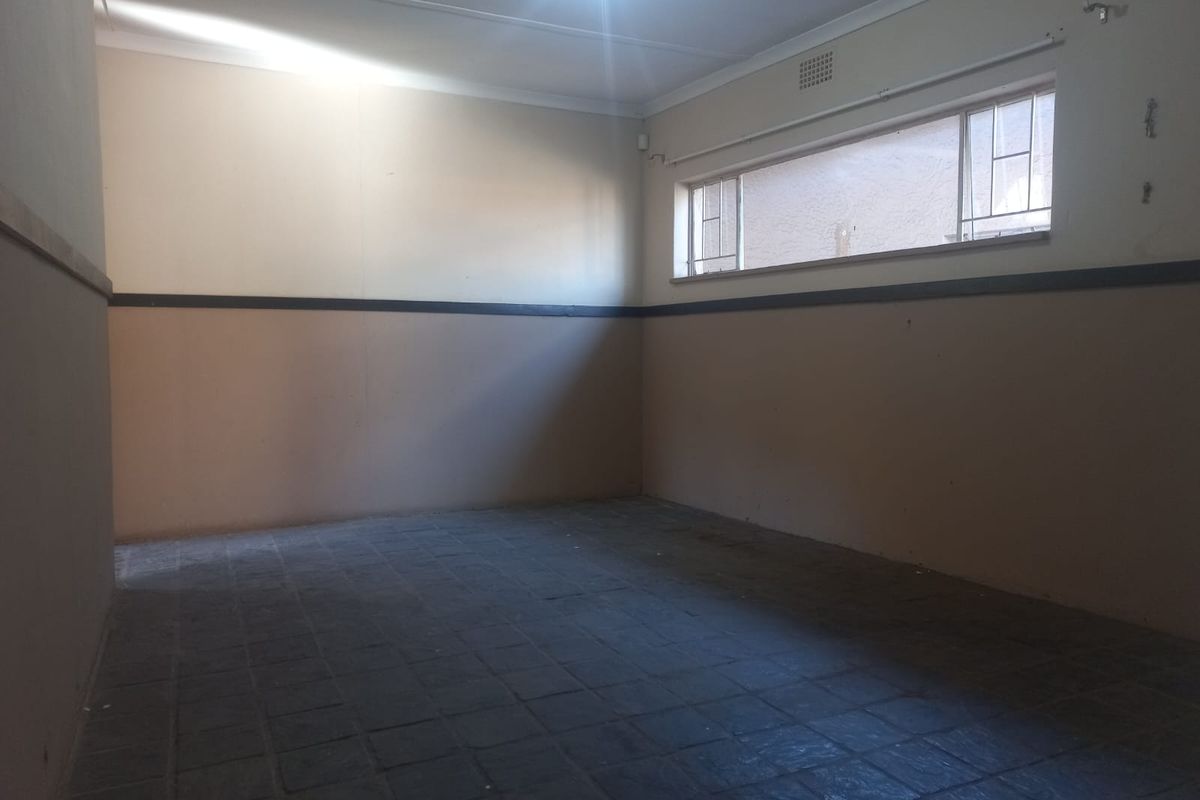 An empty, multi-purpose room featuring dark tiled flooring, two-tone wall paint, and a high-set horizontal window providing natural light.