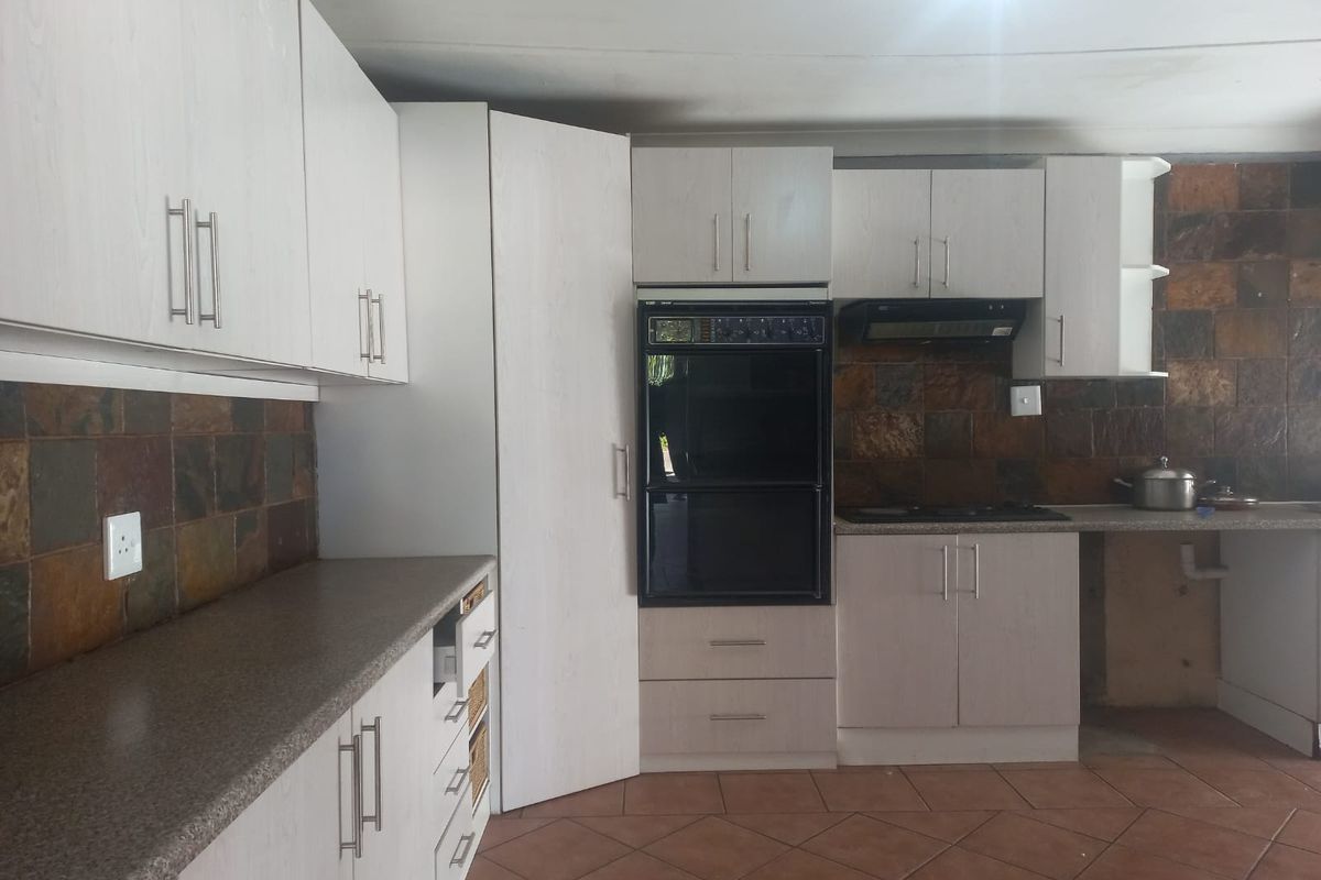 A functional kitchen featuring light-toned cabinetry, a built-in double oven, a dark stone-style backsplash, and tiled flooring.