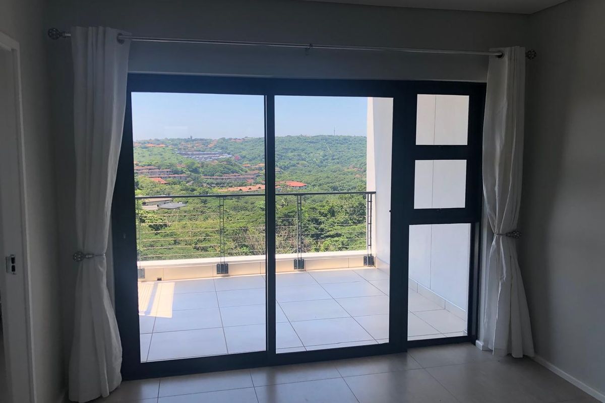 Bright living area featuring large sliding glass doors that open onto a private balcony with scenic hillside views.