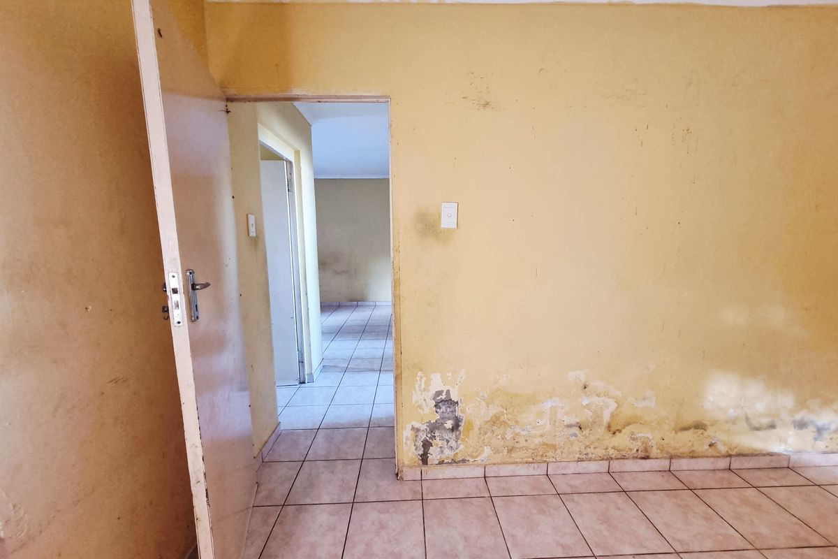 An empty room featuring tiled flooring and yellow walls showing significant signs of wear, moisture damage, and peeling paint, requiring refurbishment.