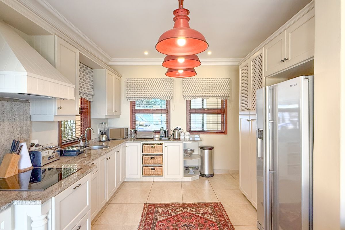 A well-maintained kitchen featuring granite countertops, ample built-in cabinetry, an induction cooktop, and a dedicated extractor fan with modern pendant lighting.