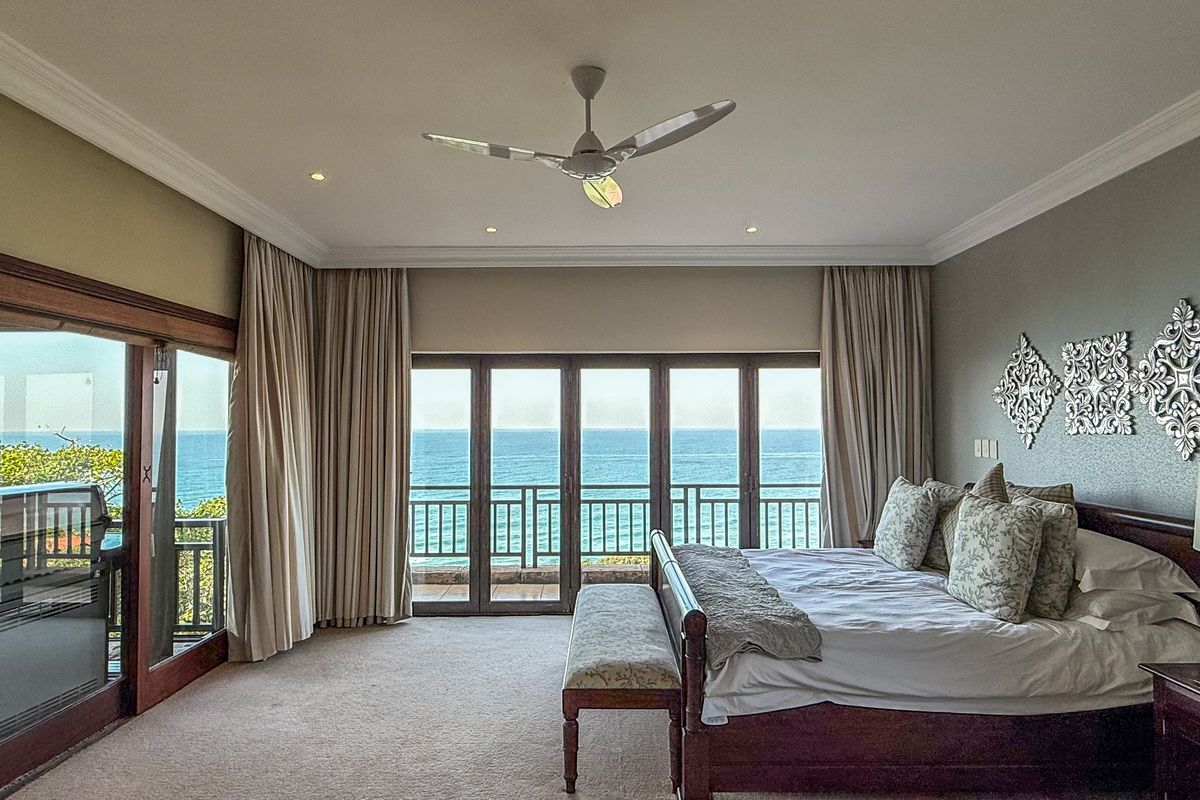 Spacious bedroom featuring crown molding, a ceiling fan, and large sliding glass doors that open to a balcony with expansive ocean views.