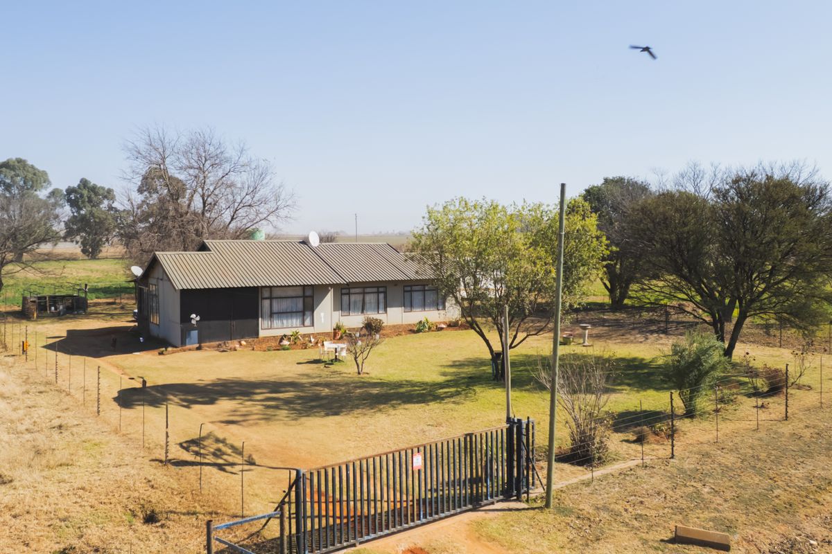 An aerial view of a farm property featuring a single-story residence, expansive garden, and secure gated entrance.