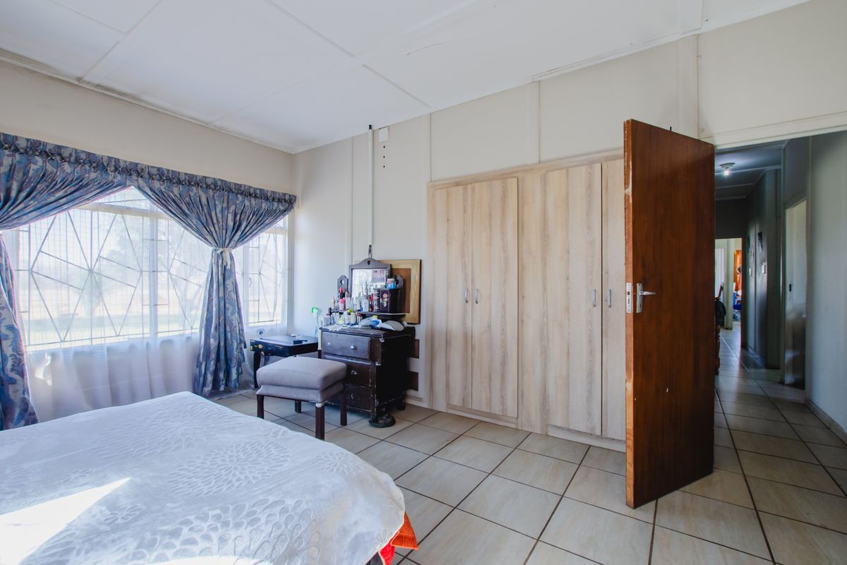 A bedroom featuring tiled flooring, built-in wooden cabinetry, and large windows with security bars, providing natural light and access to an adjacent hallway.