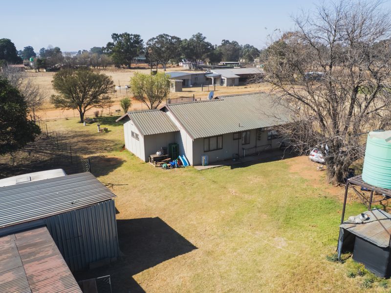 Aerial view of a farm property featuring a main dwelling with a metal roof, a secondary outbuilding, and a raised water storage tank.