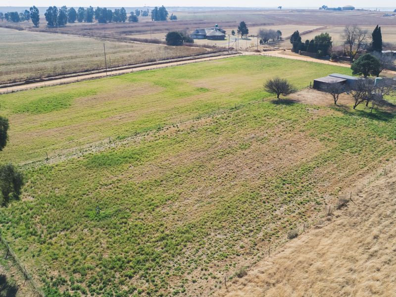 An aerial view of a large farm property featuring open grazing land, perimeter fencing, and existing outbuildings set within a rural landscape.