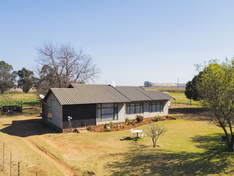 Aerial view of a single-story farmhouse featuring a corrugated metal roof, large windows, and surrounding open farmland.