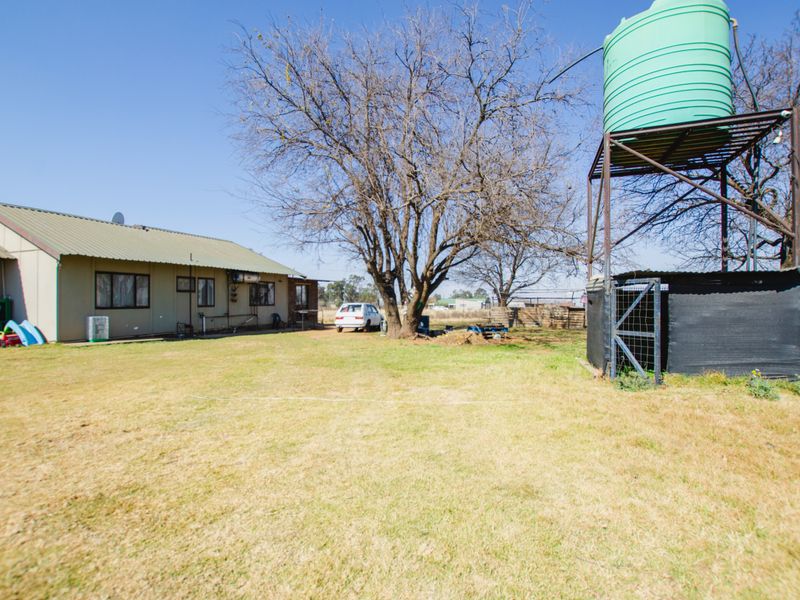 Rear view of the farm property featuring a large water storage tank on a metal stand and a spacious grass yard.