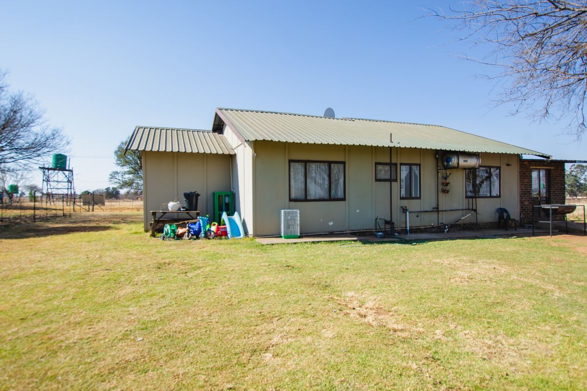 Rear view of a farm dwelling featuring metal roof sheeting, exterior wall cladding, and a water tank structure in the distance.