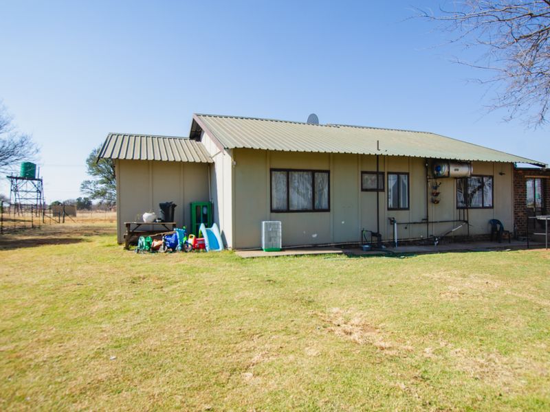 Rear view of a farm dwelling featuring metal roof sheeting, exterior wall cladding, and a water tank structure in the distance.
