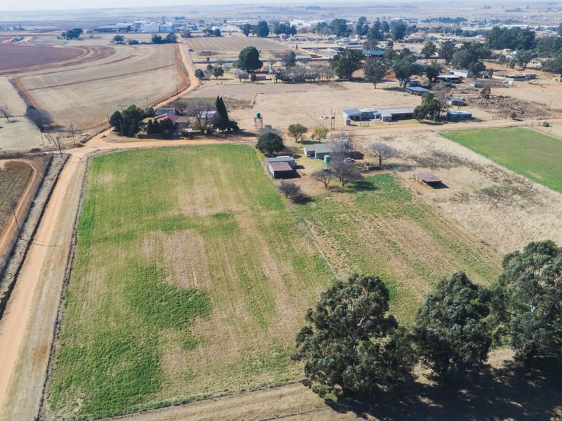 Aerial view of a large farm property featuring open grazing land, multiple outbuildings, and established trees in a rural setting.