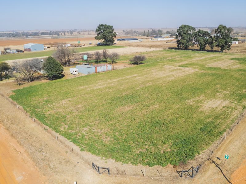 Aerial view of a large, open farm plot featuring perimeter fencing, mature trees, and small utility structures on the property.