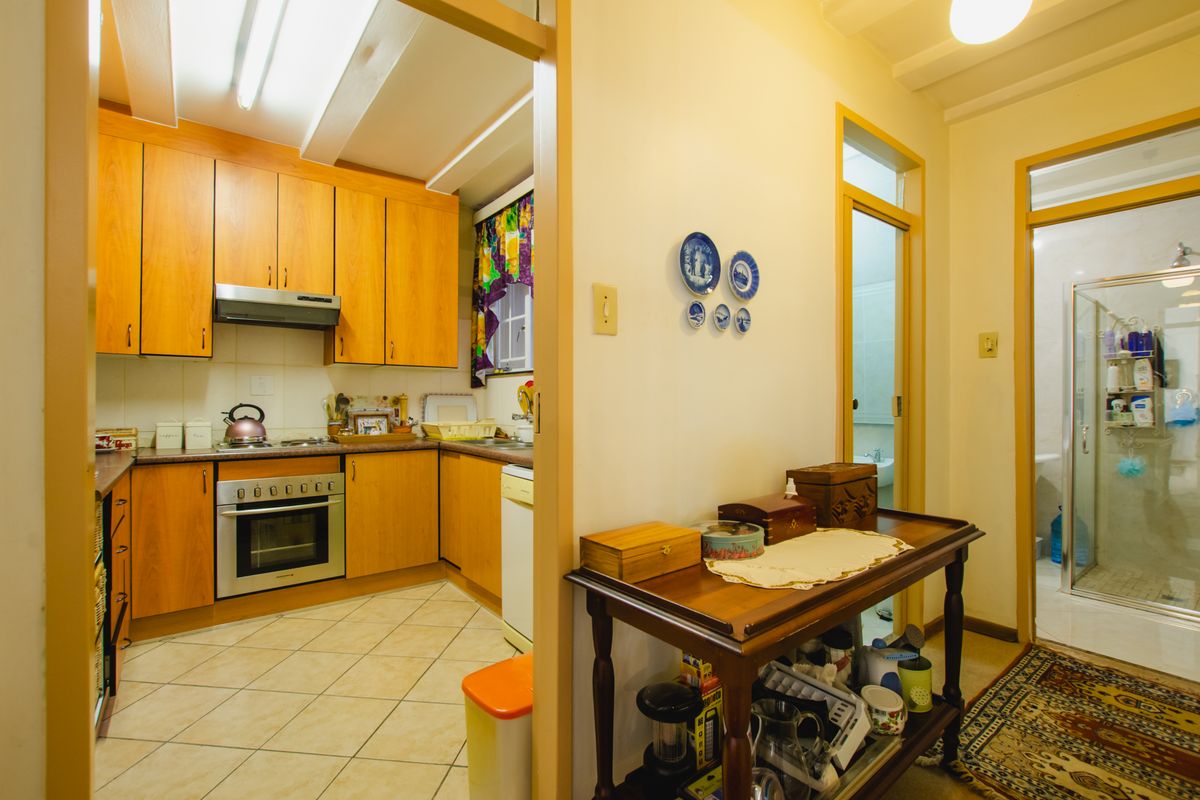 A view from a hallway into a kitchen featuring wooden cabinetry, a built-in oven, and a tiled floor, with an adjacent bathroom entrance.