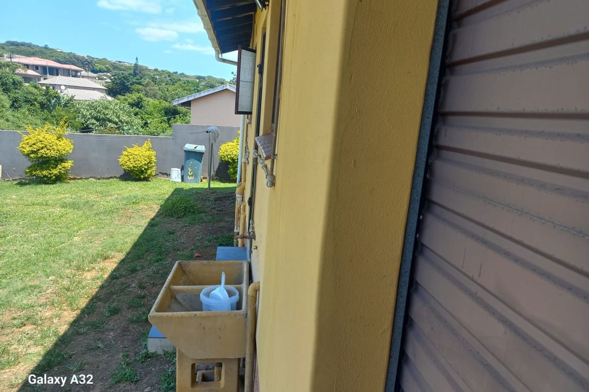 Exterior view of the side of the house featuring a concrete utility sink, downspout, and roller shutter door leading to the rear garden area.