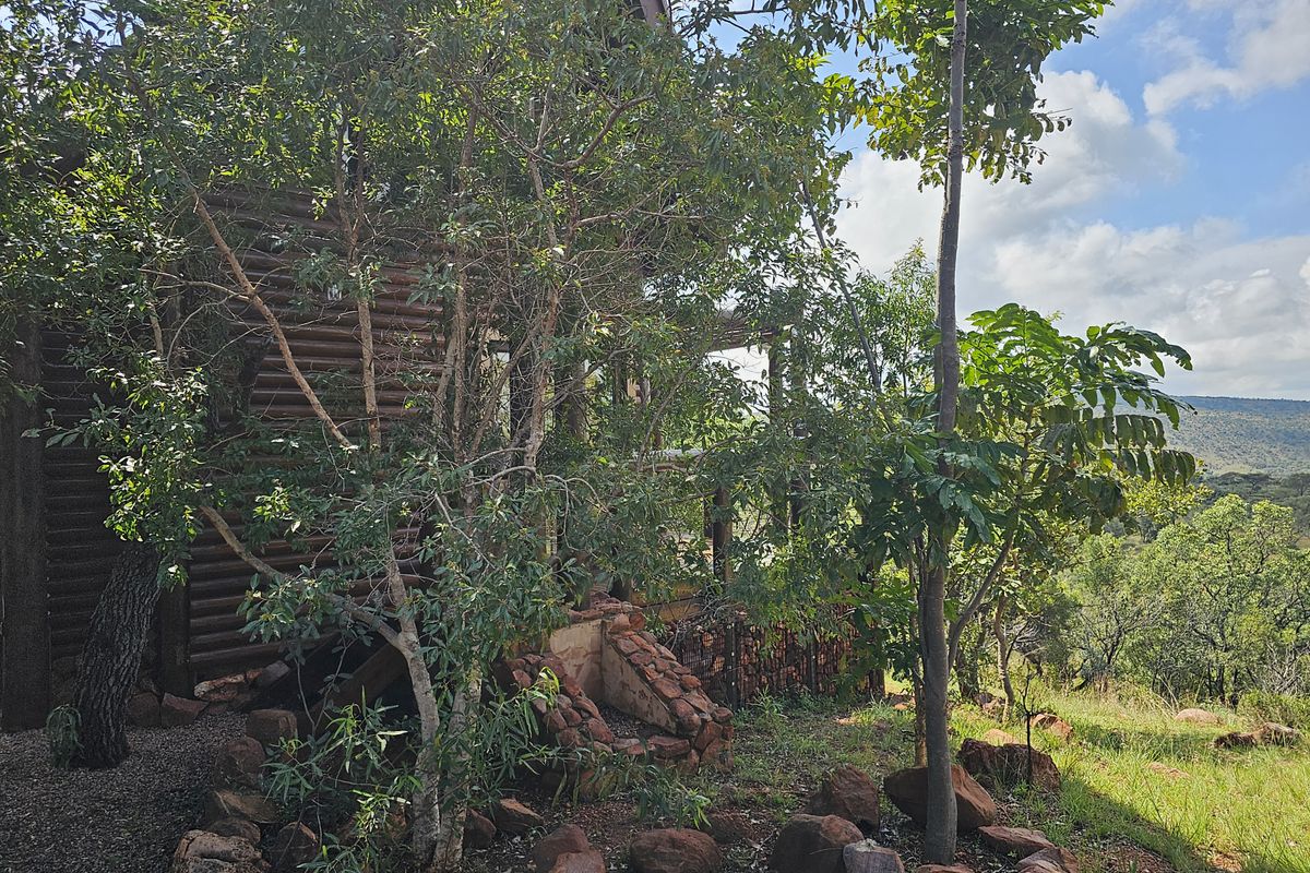 A view of the exterior rear of the property, featuring natural stone landscaping and a wooden structure nestled within a scenic, elevated bushveld setting.