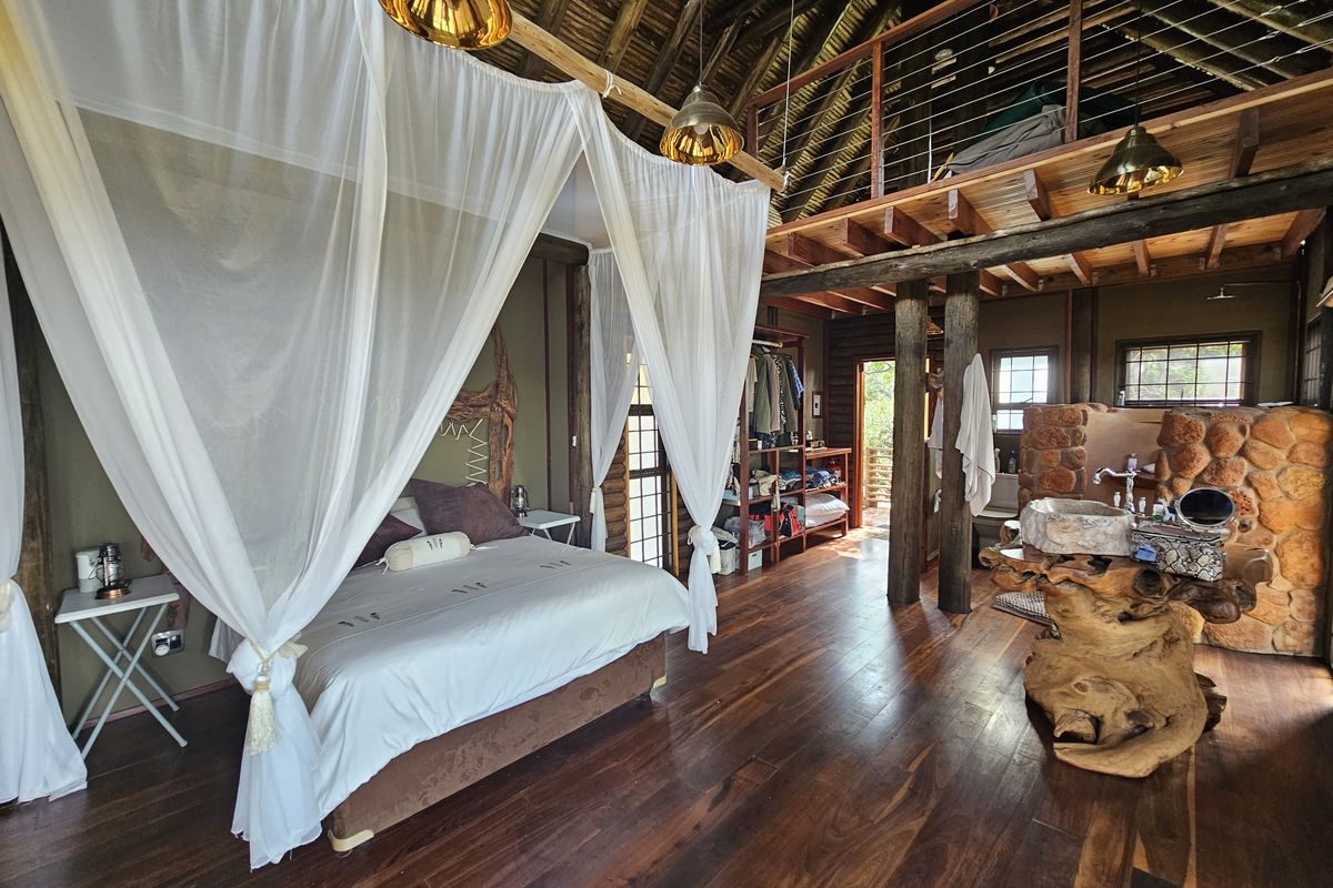 Unique open-plan bedroom featuring a thatched roof, timber flooring, mezzanine level, and a rustic stone-clad vanity area with a natural wood basin.