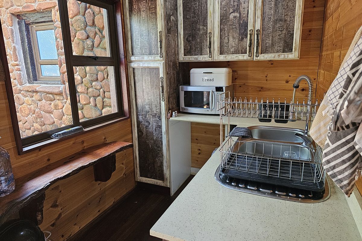 Compact kitchen area featuring rustic timber wall paneling, stone-clad exterior window view, stone-look countertops, and custom printed cabinetry.