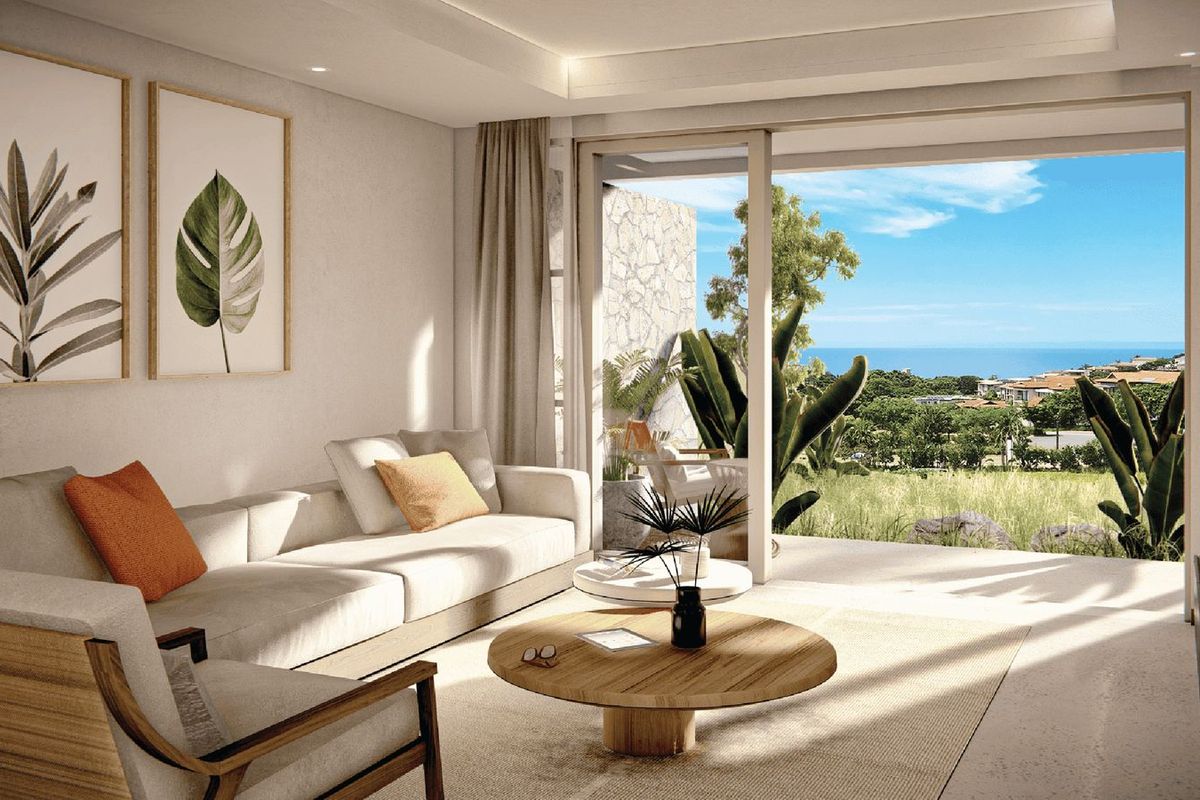 A bright, modern living room featuring large sliding glass doors that open onto a patio with scenic coastal views.