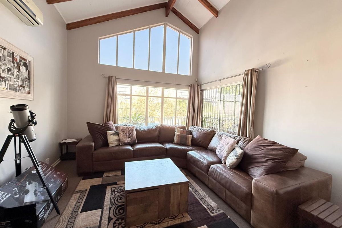 Spacious living room featuring high vaulted ceilings with exposed timber beams, large windows, and a split-system air conditioning unit.