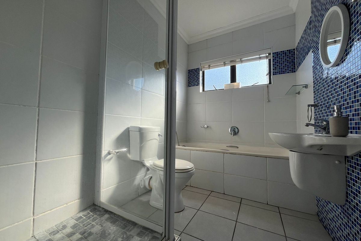 A functional bathroom featuring a glass-enclosed shower, a built-in bathtub, a pedestal sink, and blue mosaic tile accents.