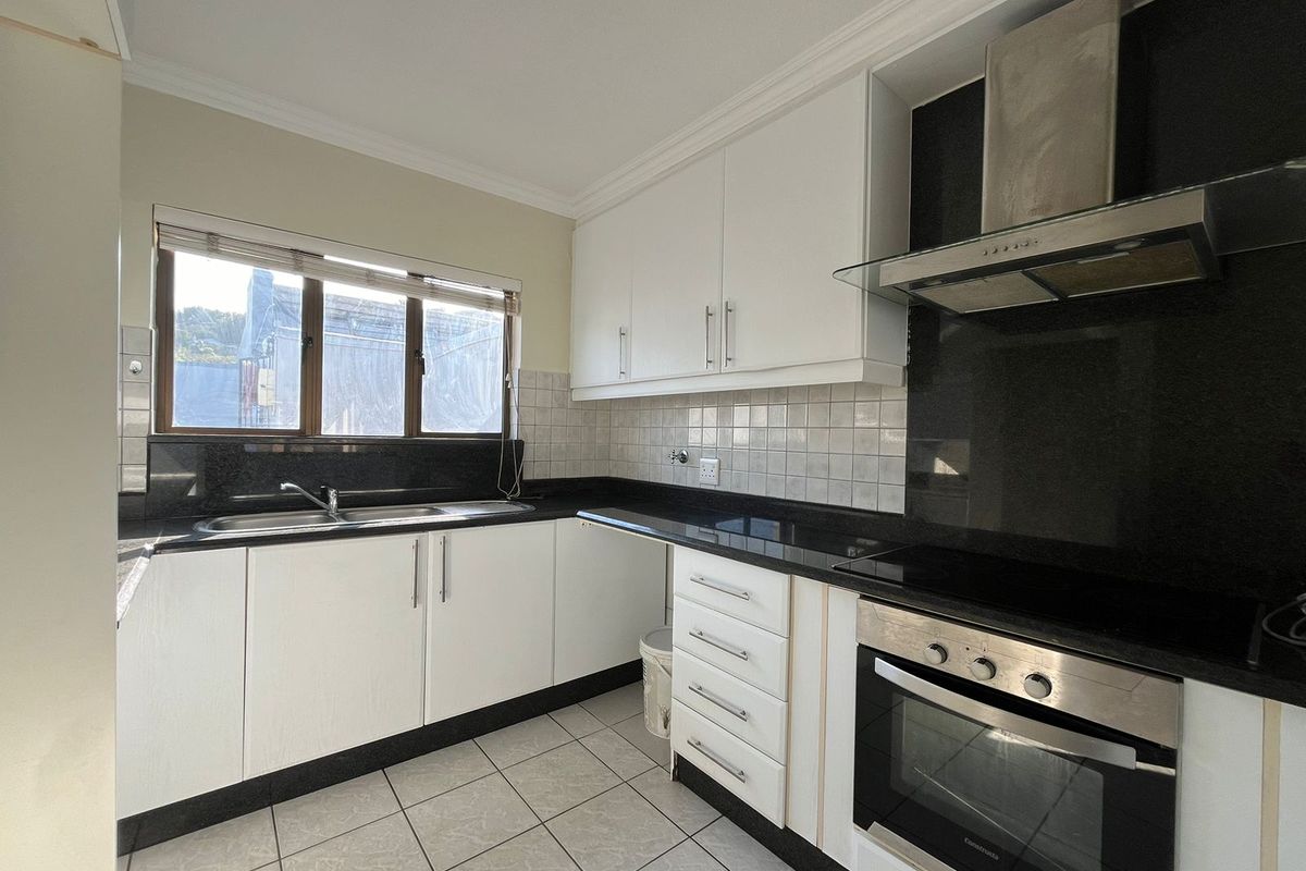 A functional kitchen featuring white cabinetry, black granite countertops, a built-in oven, extractor fan, and tiled flooring with a double sink.