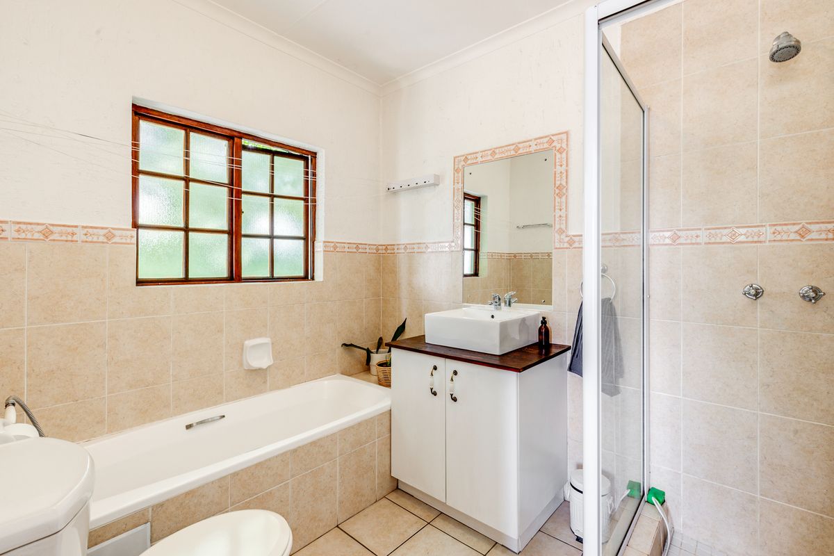 A functional bathroom featuring a bathtub, a separate glass-enclosed shower, a vanity with a vessel sink, and a window for natural light.