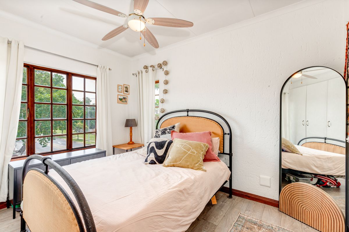 A bright bedroom featuring timber-framed windows, a ceiling fan, and built-in cupboards, offering a comfortable and functional living space.