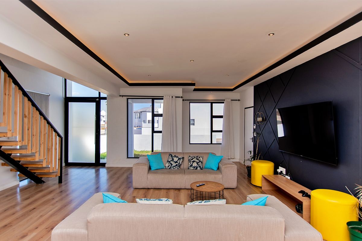 Modern open-plan living area featuring a striking feature wall, timber staircase, recessed ceiling lighting, and large windows providing ample natural light.