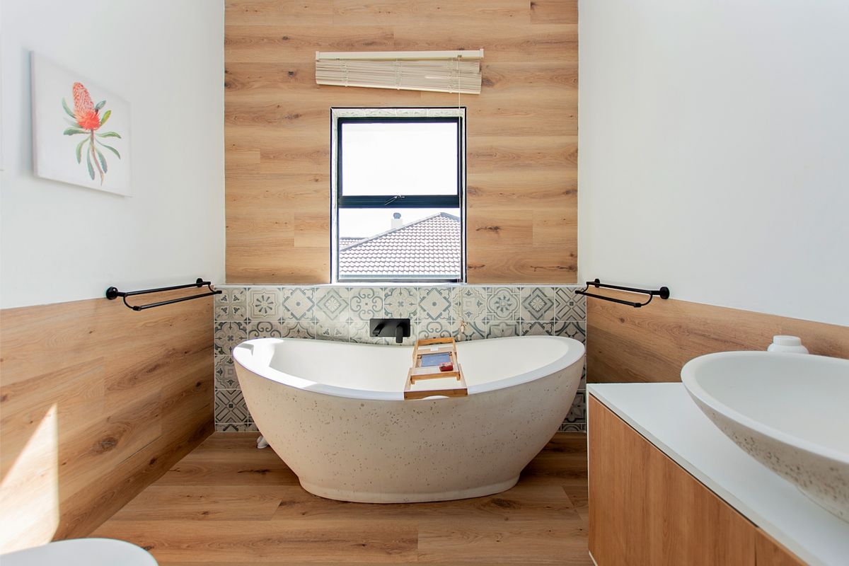 Modern bathroom featuring a contemporary freestanding bathtub, timber-look wall accents, patterned tile splashback, and sleek black matte fixtures.