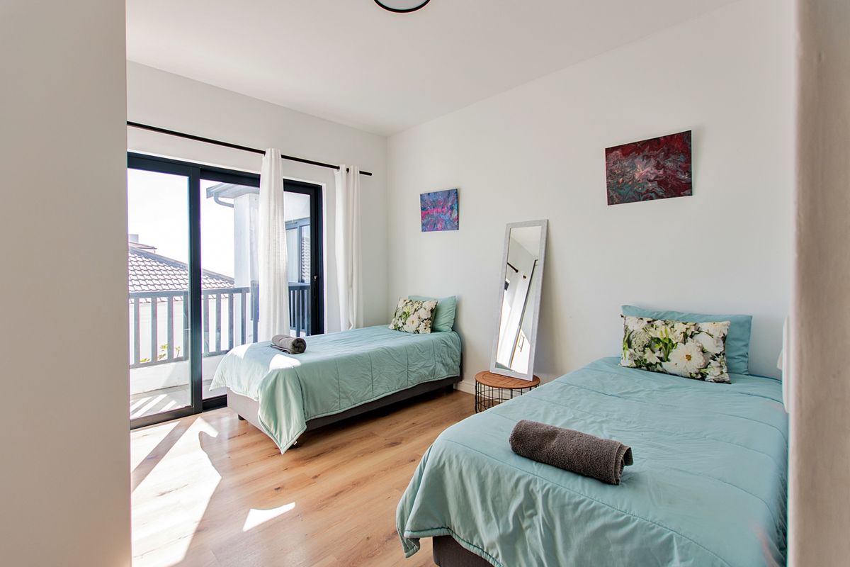 A bright bedroom featuring laminate flooring and a large sliding glass door providing direct access to an outdoor balcony.