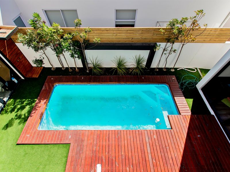 An elevated view of a private courtyard featuring a swimming pool surrounded by timber decking, artificial turf, and a modern privacy screen.