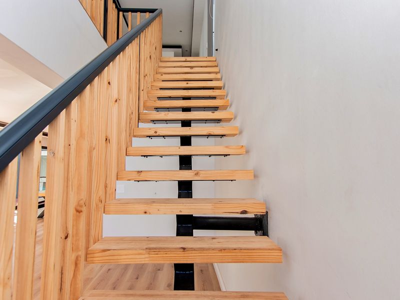 Modern open-riser timber staircase featuring a sleek black metal handrail and balustrade, connecting levels with a contemporary architectural aesthetic.