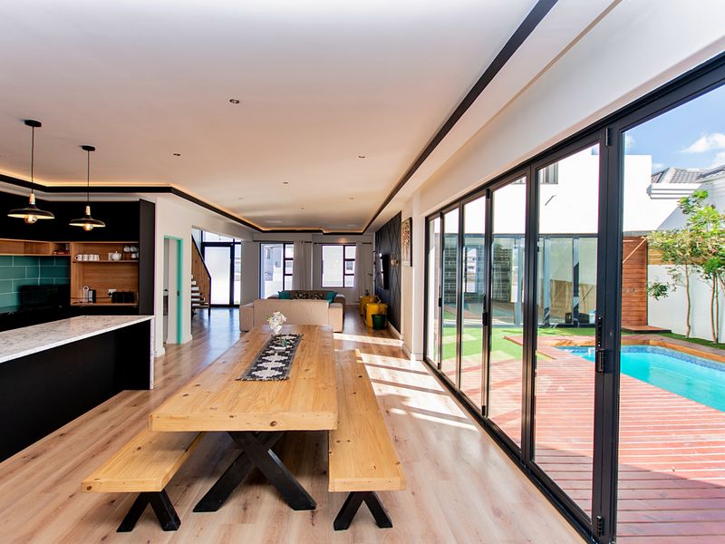 Modern open-plan living area featuring a sleek kitchen, dining space, and seamless indoor-outdoor flow through large bi-fold doors to the pool deck.