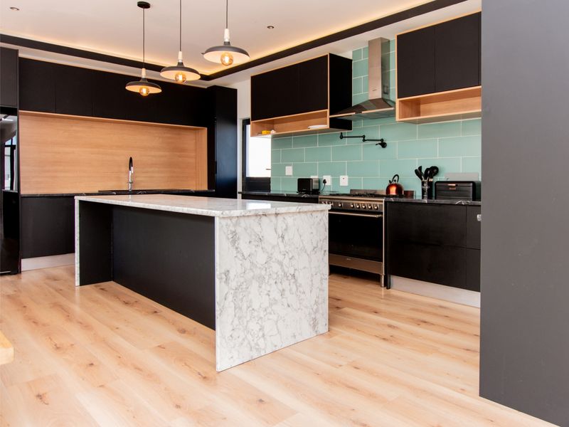 Modern kitchen featuring a marble-topped island, sleek black cabinetry, light wood flooring, and a stylish teal subway tile backsplash.