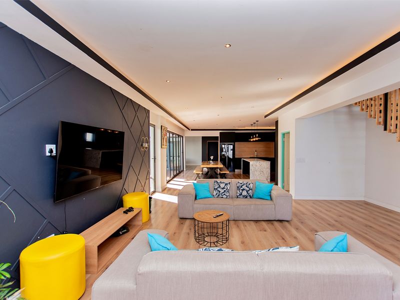 Spacious open-plan living area featuring modern timber flooring, a striking feature wall, recessed lighting, and a seamless transition to the contemporary kitchen.