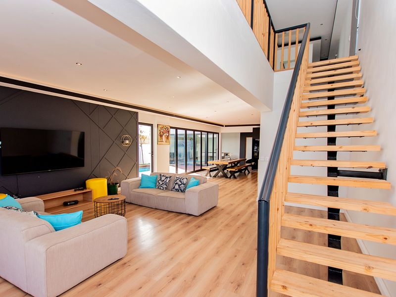 Spacious open-plan living area featuring modern timber staircase, laminate flooring, recessed lighting, and large bi-fold doors leading to the outdoor space.