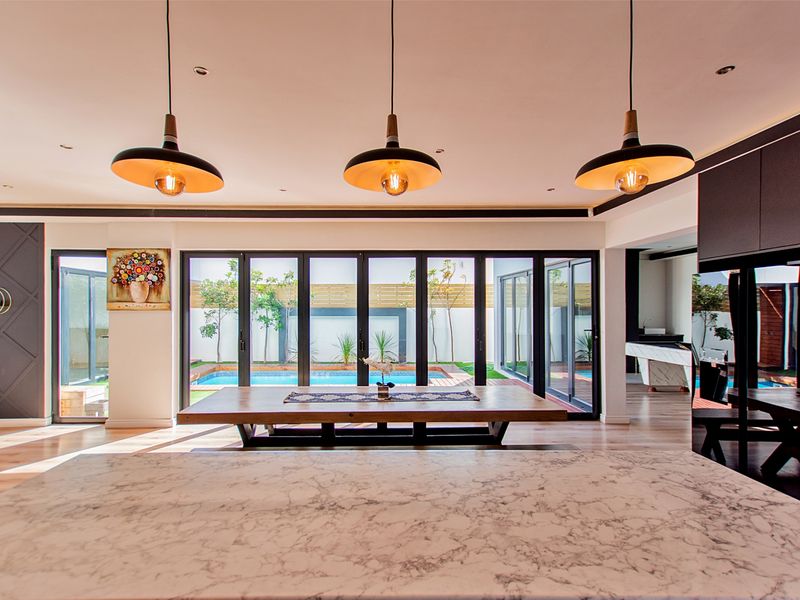 Spacious open-plan living area featuring a marble kitchen island, modern pendant lighting, and seamless bi-fold doors opening to a private pool and garden.