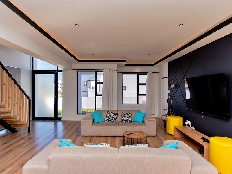 Modern open-plan living area featuring a striking feature wall, timber staircase, recessed ceiling lighting, and large windows providing ample natural light.