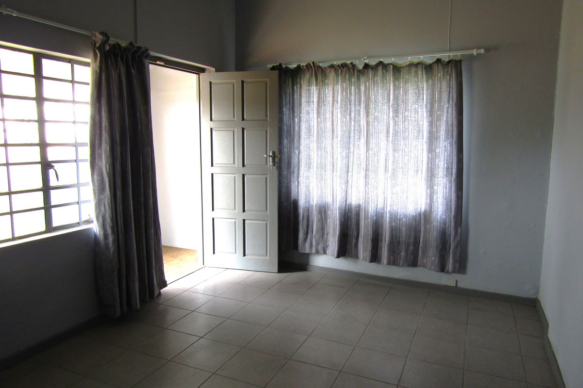 An empty bedroom featuring tiled flooring, a steel-framed window, and a panel door, offering a blank canvas for renovation.